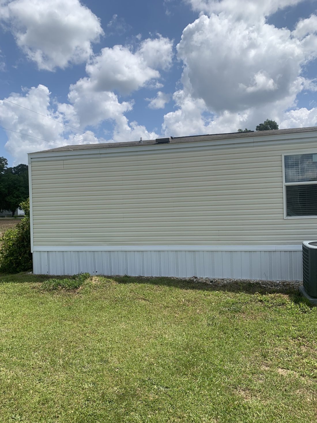 A long wall of cleaned vinyl siding with a window under a blue sky